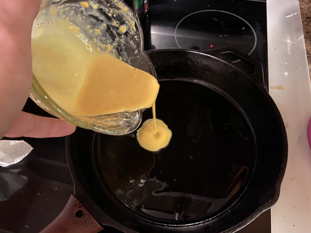 A photo of Josh pouring the egg mix into a cast-iron skillet