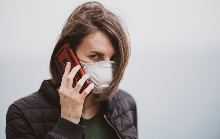 A woman wearing a valved respirator and talking on a cell phone