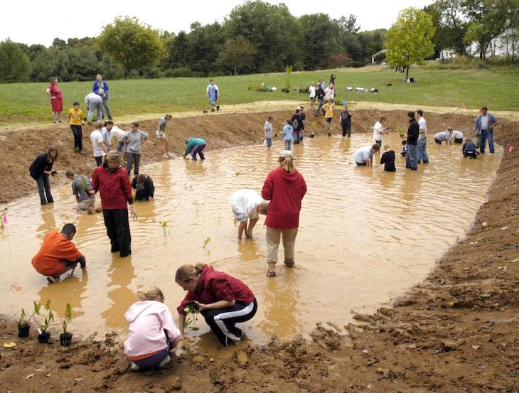 People milling around a muddy pond